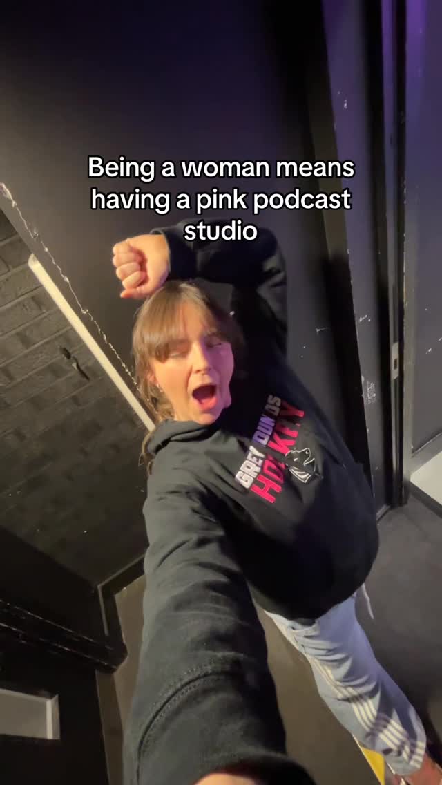 Emma celebrating outside the pink Her Game, Her Voice podcast studio